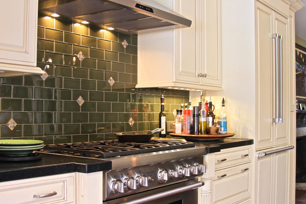 Medelhavsstil inredning av ett mellanstort kök, med luckor med upphöjd panel, vita skåp, granitbänkskiva, grönt stänkskydd, stänkskydd i keramik, rostfria vitvaror, en undermonterad diskho, mellanmörkt trägolv och en köksö
