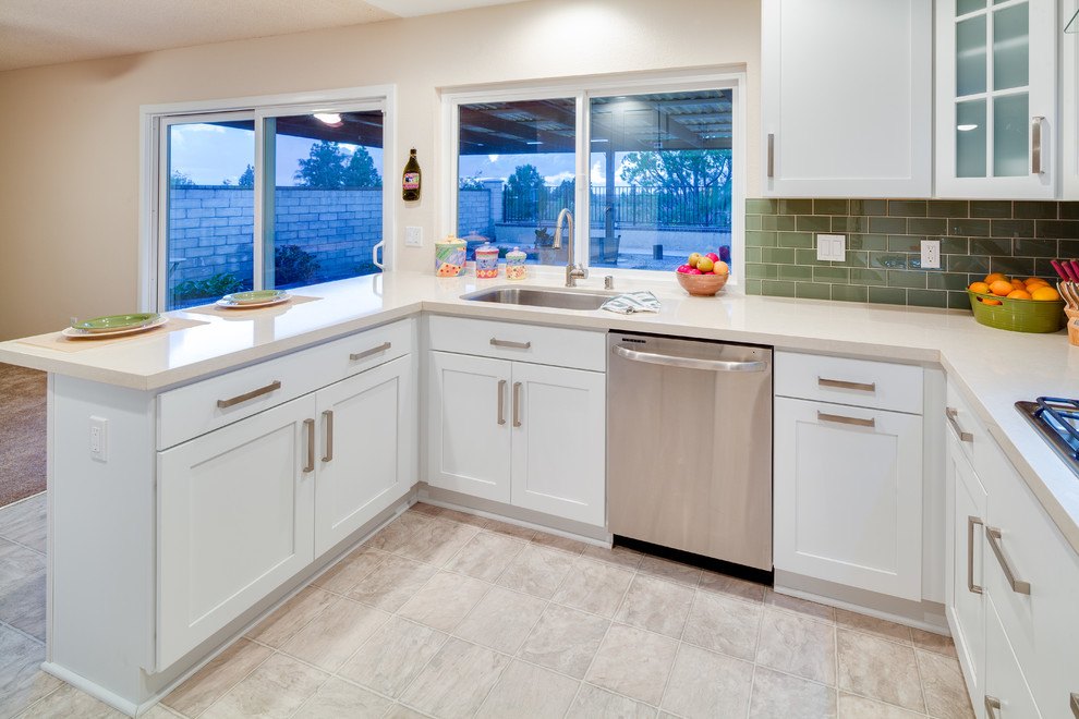 Design ideas for a traditional u-shaped kitchen/diner in San Diego with a built-in sink, glass-front cabinets, white cabinets, green splashback, metro tiled splashback and stainless steel appliances.