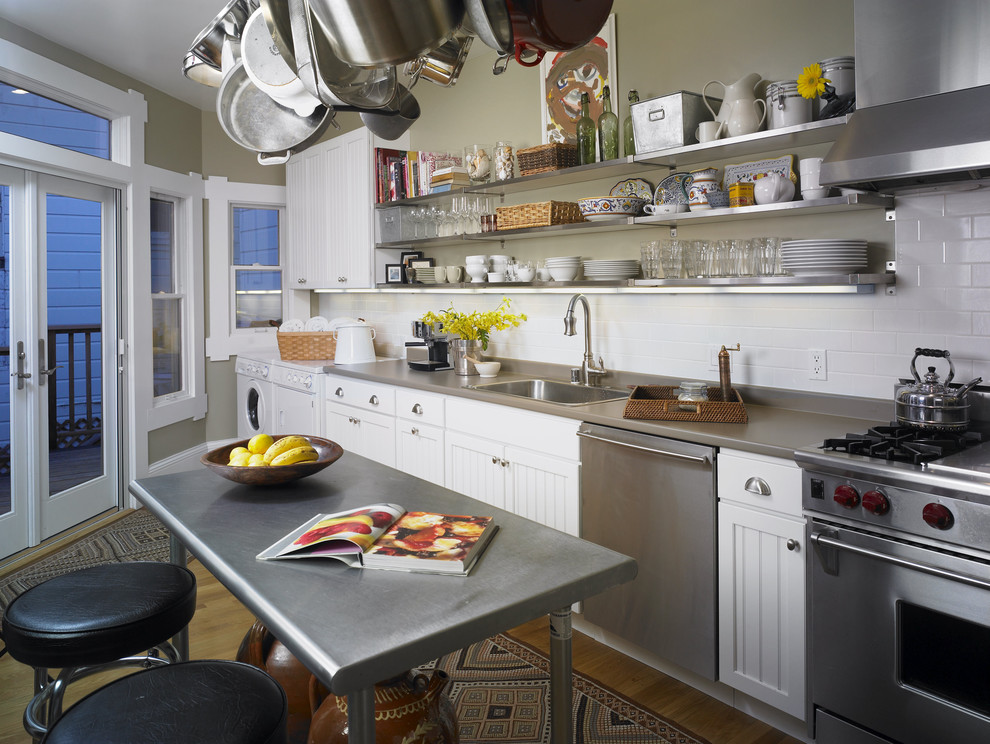 Example of a mid-sized eclectic galley light wood floor eat-in kitchen design in San Francisco with subway tile backsplash, a drop-in sink, beaded inset cabinets, white cabinets, white backsplash, stainless steel appliances, an island and solid surface countertops