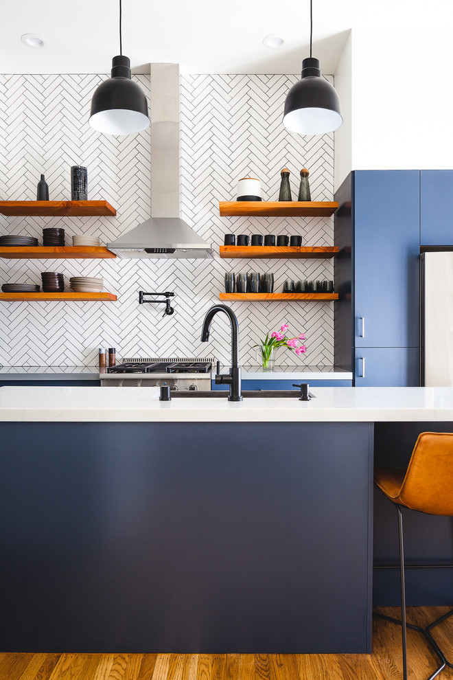 Идея дизайна: параллельная кухня в современном стиле с плоскими фасадами, синими фасадами, белым фартуком, фартуком из плитки мозаики, техникой из нержавеющей стали, паркетным полом среднего тона, островом, коричневым полом и белой столешницей