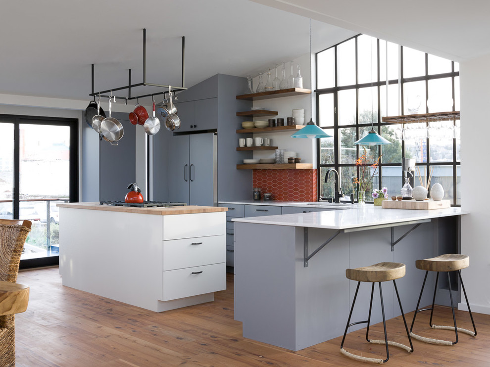 Cette photo montre une cuisine ouverte encastrable moderne en L avec plan de travail en marbre, un placard à porte plane, des portes de placard bleues, une crédence rouge et une crédence en céramique.