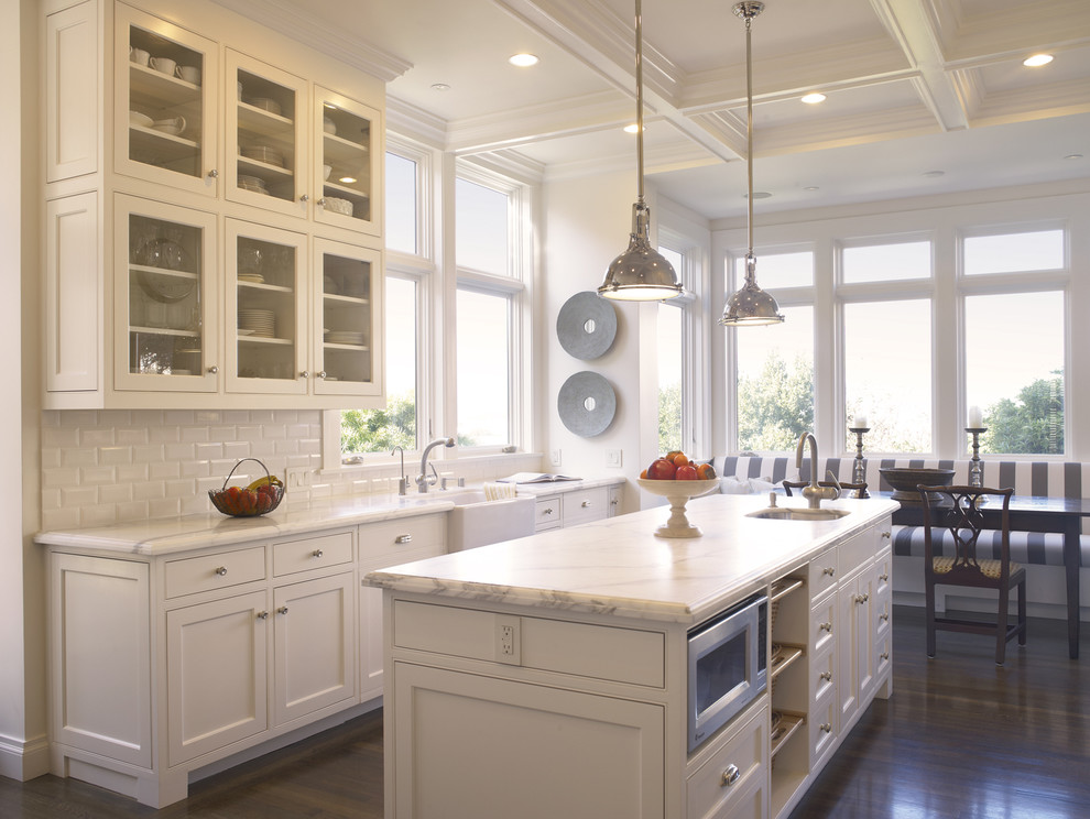 Example of a classic eat-in kitchen design in San Francisco with subway tile backsplash, a farmhouse sink, glass-front cabinets, white cabinets, white backsplash and marble countertops