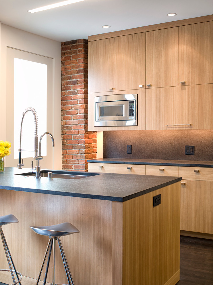 Example of a mid-sized urban galley dark wood floor and brown floor eat-in kitchen design in San Francisco with an undermount sink, flat-panel cabinets, light wood cabinets, stainless steel appliances, an island, brown backsplash, stone slab backsplash and solid surface countertops