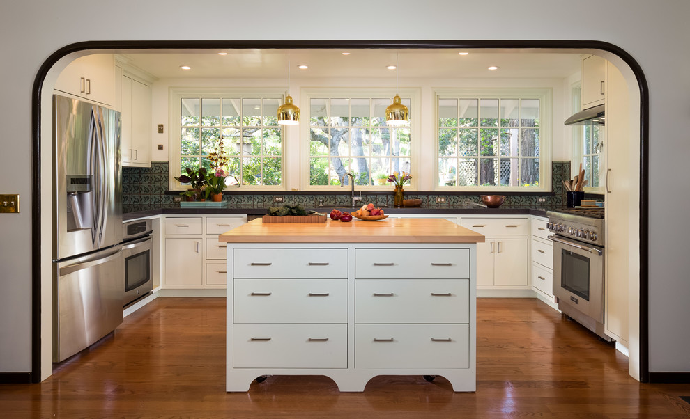 Inspiration for a medium sized classic u-shaped enclosed kitchen in San Francisco with a double-bowl sink, stainless steel appliances, medium hardwood flooring, an island, brown floors, flat-panel cabinets, white cabinets, green splashback and black worktops.