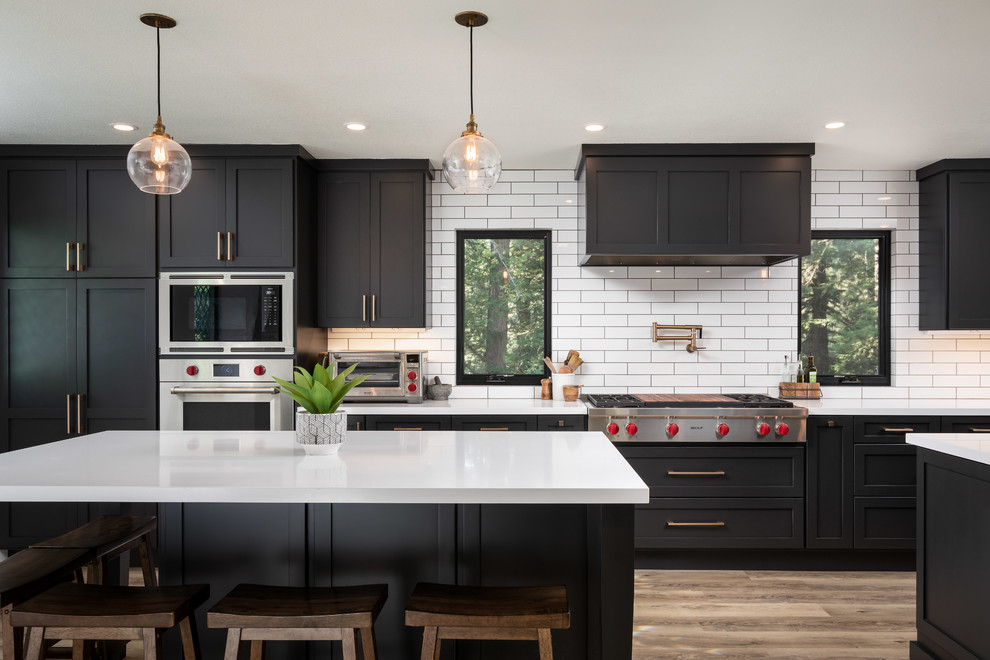 Example of a large transitional brown floor and medium tone wood floor open concept kitchen design in San Francisco with a drop-in sink, flat-panel cabinets, black cabinets, granite countertops, white backsplash, subway tile backsplash, stainless steel appliances, two islands and white countertops