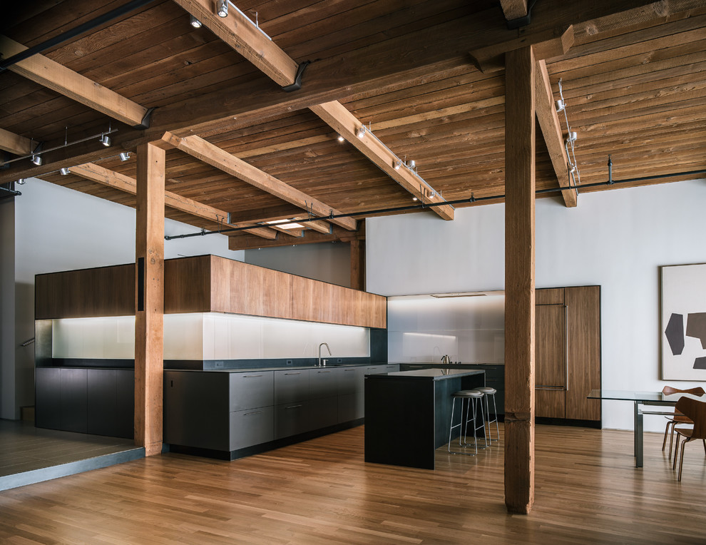 Zweizeilige Industrial Wohnküche mit flächenbündigen Schrankfronten, hellbraunen Holzschränken, Küchenrückwand in Schwarz und Elektrogeräten mit Frontblende in San Francisco