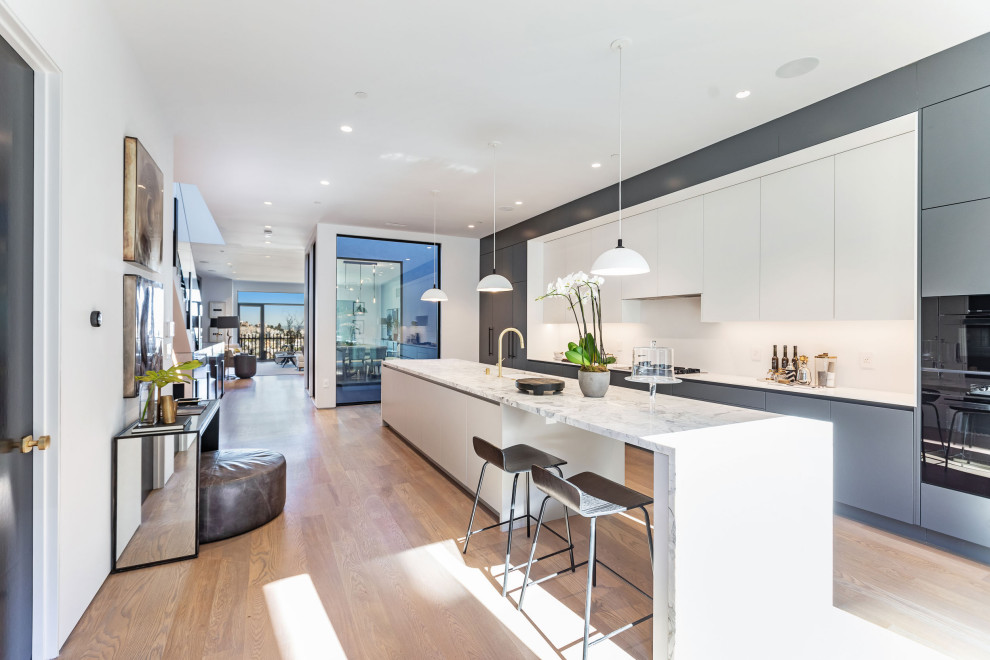 Esempio di una cucina design con ante lisce, ante grigie, elettrodomestici neri, pavimento in legno massello medio, pavimento marrone e top bianco