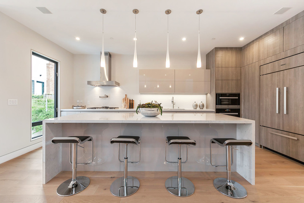 This is an example of a contemporary kitchen in San Francisco with flat-panel cabinets, beige cabinets, integrated appliances, light hardwood flooring and an island.