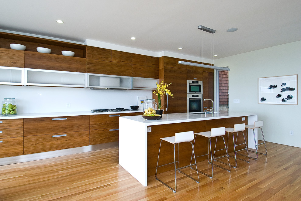 Exemple d'une cuisine ouverte linéaire moderne en bois brun de taille moyenne avec un évier 1 bac, un placard à porte plane, une crédence blanche, un électroménager en acier inoxydable, parquet clair et îlot.