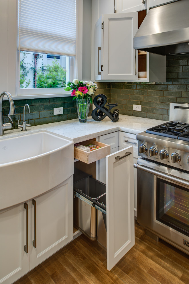 Bild på ett mellanstort vintage kök, med en rustik diskho, luckor med infälld panel, vita skåp, bänkskiva i kvarts, grått stänkskydd, stänkskydd i tunnelbanekakel, rostfria vitvaror, mellanmörkt trägolv och en halv köksö