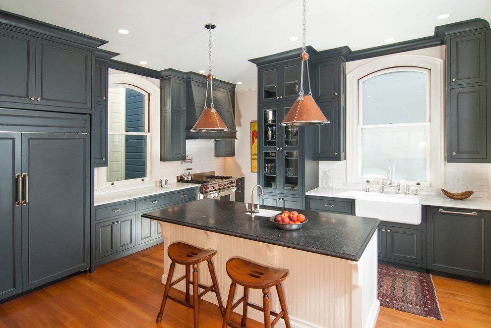 Klassisk inredning av ett avskilt, mellanstort kök, med en rustik diskho, luckor med infälld panel, grå skåp, marmorbänkskiva, vitt stänkskydd, stänkskydd i tunnelbanekakel, integrerade vitvaror, mellanmörkt trägolv och en köksö