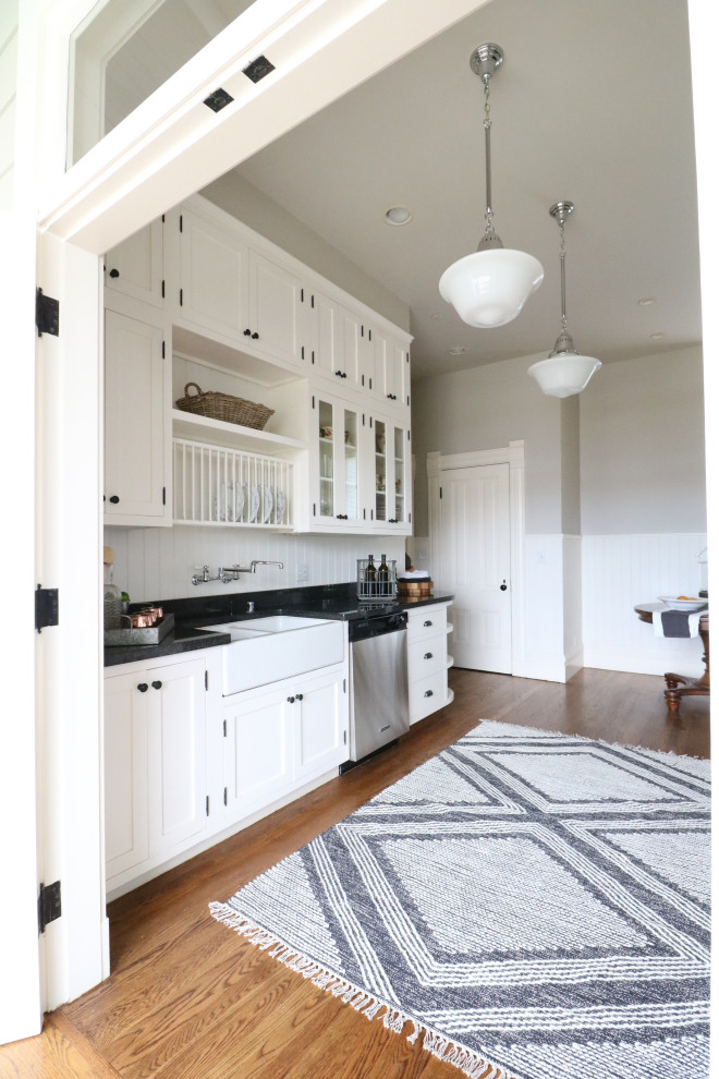 Ornate galley medium tone wood floor kitchen photo in San Francisco with a farmhouse sink, recessed-panel cabinets, white cabinets, white backsplash, wood backsplash, stainless steel appliances and black countertops