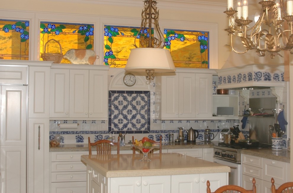 Bild på ett stort vintage u-kök, med en undermonterad diskho, luckor med infälld panel, vita skåp, granitbänkskiva, blått stänkskydd, stänkskydd i keramik, vita vitvaror och en köksö