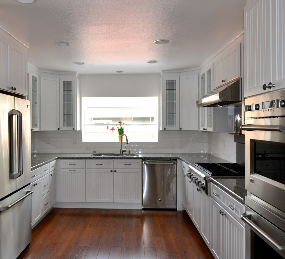 Exempel på ett klassiskt kök, med en undermonterad diskho, luckor med profilerade fronter, vita skåp, granitbänkskiva, vitt stänkskydd, stänkskydd i keramik och rostfria vitvaror