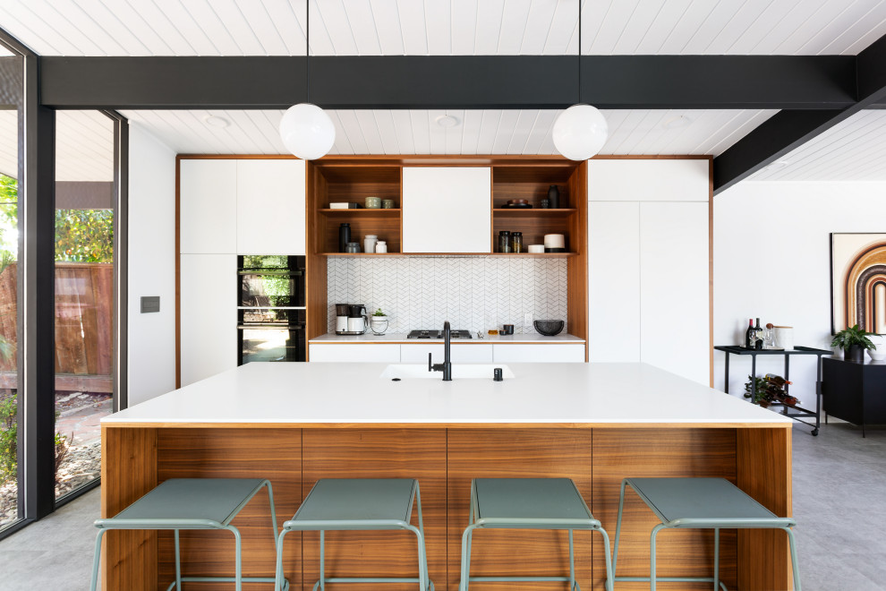 Midcentury galley kitchen in San Francisco with a submerged sink, flat-panel cabinets, white cabinets, white splashback, mosaic tiled splashback, an island, grey floors and white worktops.