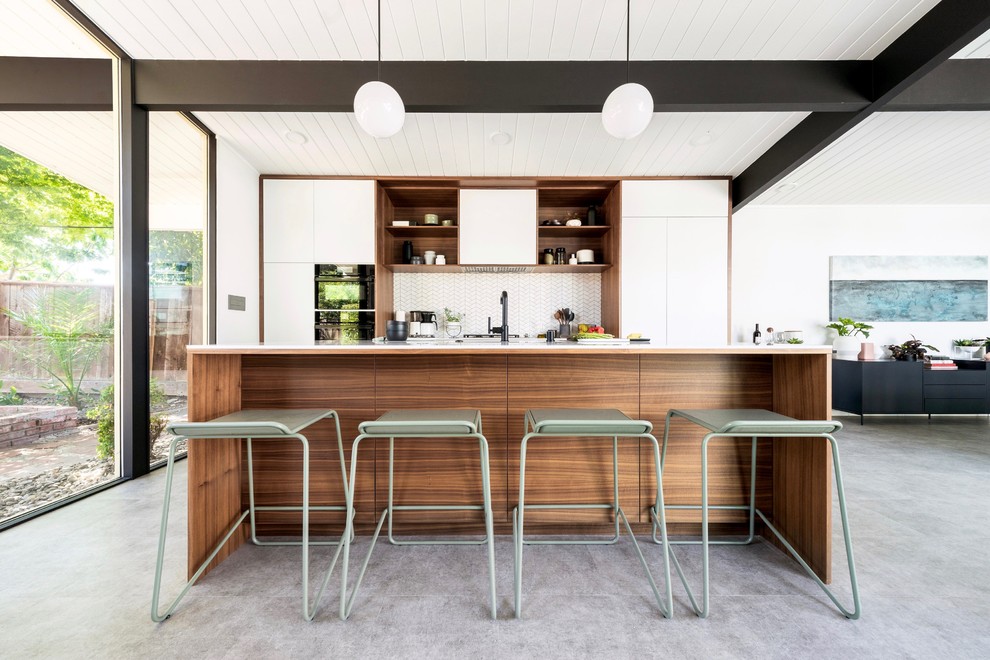 Inspiration for a midcentury galley open plan kitchen in San Francisco with flat-panel cabinets, white cabinets, white splashback, mosaic tiled splashback, integrated appliances, an island, grey floors and white worktops.