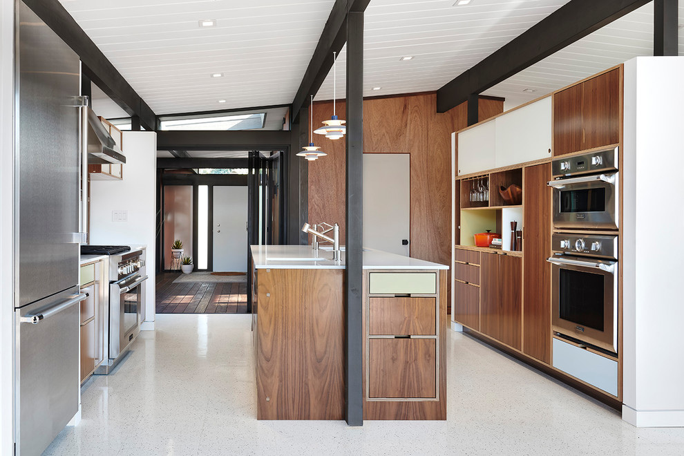 Photo of a retro kitchen in San Francisco with a submerged sink, flat-panel cabinets, medium wood cabinets, engineered stone countertops, stainless steel appliances, vinyl flooring, an island, white worktops and white floors.