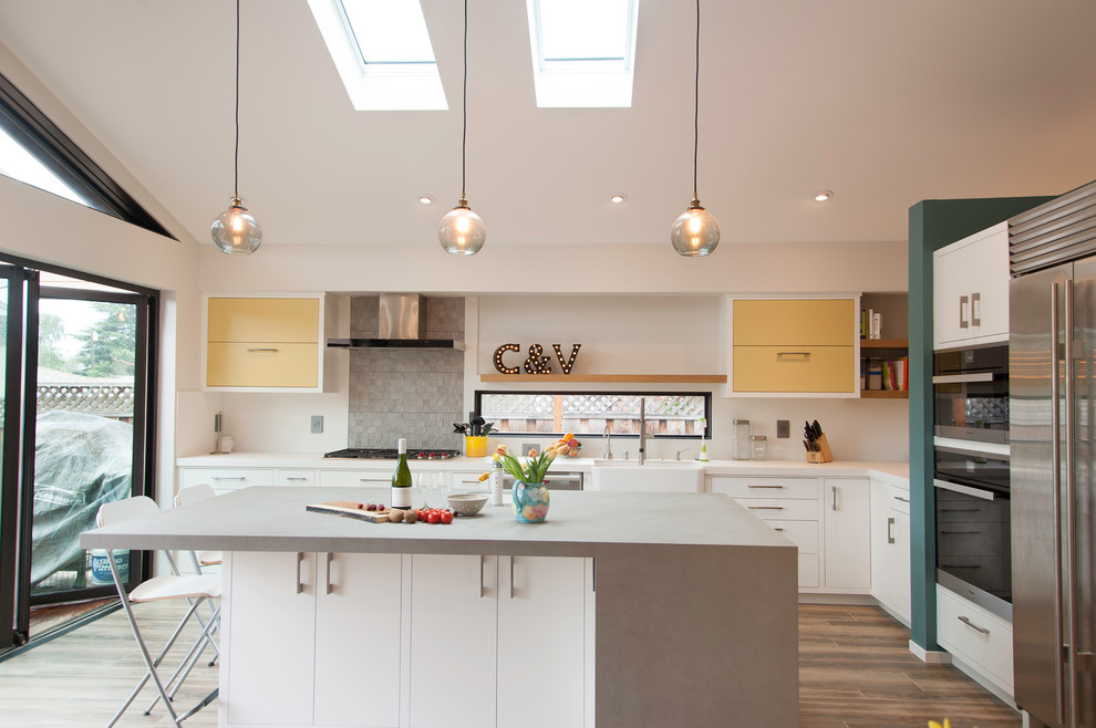 Example of a mid-sized trendy l-shaped ceramic tile open concept kitchen design in San Francisco with a farmhouse sink, recessed-panel cabinets, yellow cabinets, concrete countertops, gray backsplash, ceramic backsplash, stainless steel appliances and an island