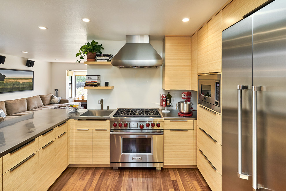 Idéer för att renovera ett funkis grå grått kök, med en integrerad diskho, släta luckor, skåp i ljust trä, bänkskiva i rostfritt stål, vitt stänkskydd, glaspanel som stänkskydd, rostfria vitvaror, mörkt trägolv, en halv köksö och brunt golv