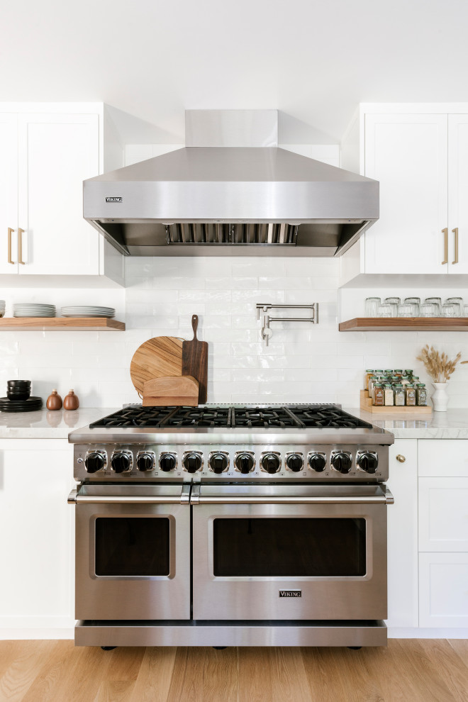 Inspiration for a mid-sized country galley light wood floor and brown floor eat-in kitchen remodel in San Francisco with an undermount sink, shaker cabinets, white cabinets, white backsplash, ceramic backsplash, stainless steel appliances, no island and white countertops