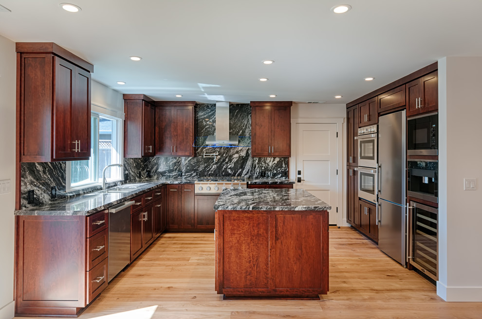 Modern inredning av ett mellanstort kök, med en dubbel diskho, luckor med infälld panel, skåp i mörkt trä, granitbänkskiva, svart stänkskydd, stänkskydd i sten, rostfria vitvaror, mellanmörkt trägolv och en köksö