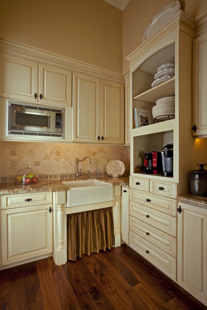 Mid-sized tuscan l-shaped medium tone wood floor kitchen pantry photo in Orange County with raised-panel cabinets, granite countertops and stone tile backsplash
