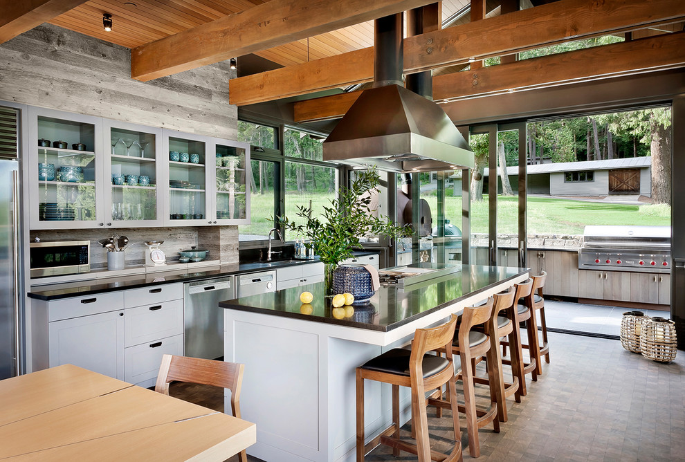 This is an example of a large rustic galley kitchen/diner in Seattle with a submerged sink, shaker cabinets, white cabinets, granite worktops, beige splashback, stainless steel appliances, dark hardwood flooring, an island, black worktops and brown floors.