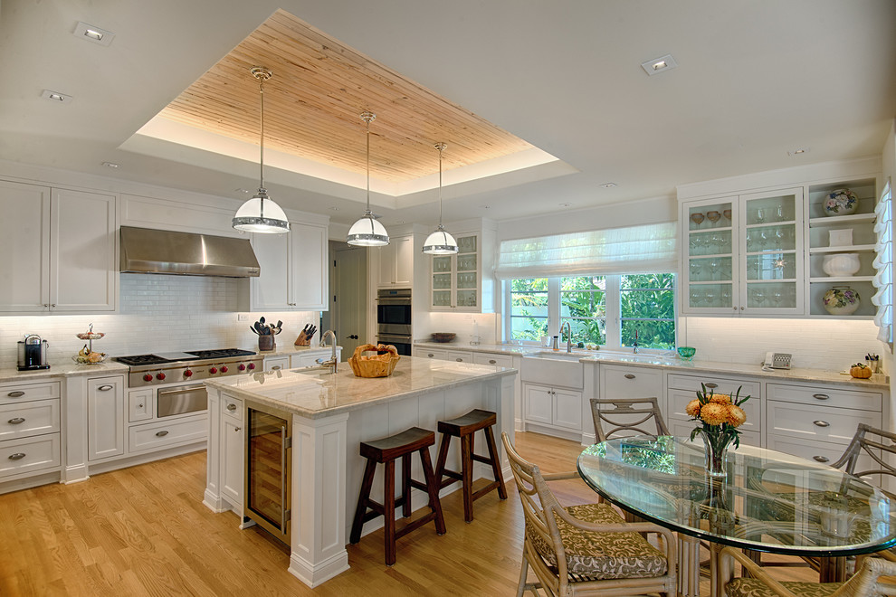 Example of a large tuscan u-shaped medium tone wood floor open concept kitchen design in Miami with a farmhouse sink, recessed-panel cabinets, white backsplash, subway tile backsplash, stainless steel appliances and an island