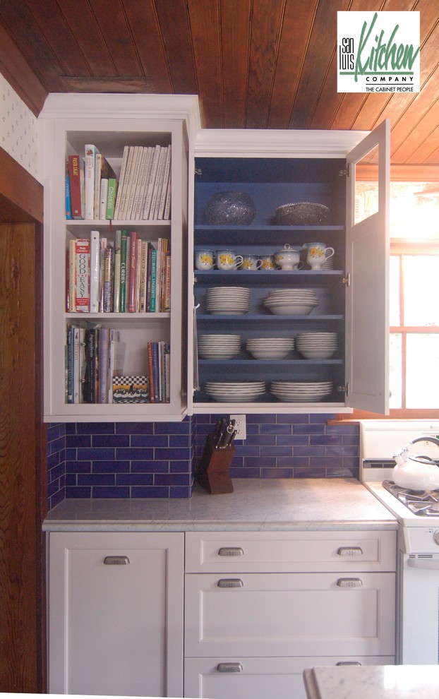 На фото: прямая кухня в классическом стиле с обеденным столом, с полувстраиваемой мойкой (с передним бортиком), фасадами с утопленной филенкой, белыми фасадами, мраморной столешницей, синим фартуком, фартуком из стеклянной плитки и белой техникой с