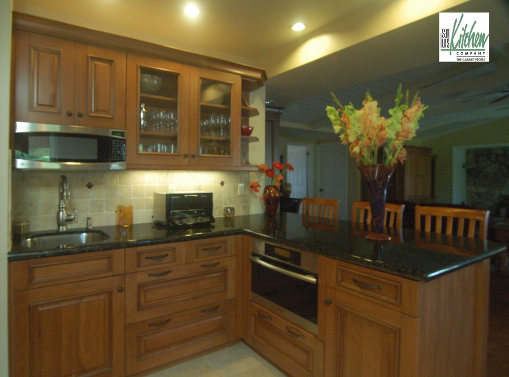 Bild på ett eklektiskt kök, med en undermonterad diskho, luckor med upphöjd panel, skåp i mellenmörkt trä, granitbänkskiva, grönt stänkskydd, stänkskydd i keramik och rostfria vitvaror