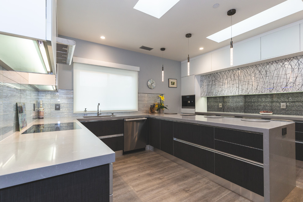 Inredning av ett modernt avskilt, mellanstort grå grått u-kök, med en undermonterad diskho, släta luckor, grå skåp, bänkskiva i kvarts, stänkskydd med metallisk yta, stänkskydd i glaskakel, rostfria vitvaror, mellanmörkt trägolv, en halv köksö och brunt golv