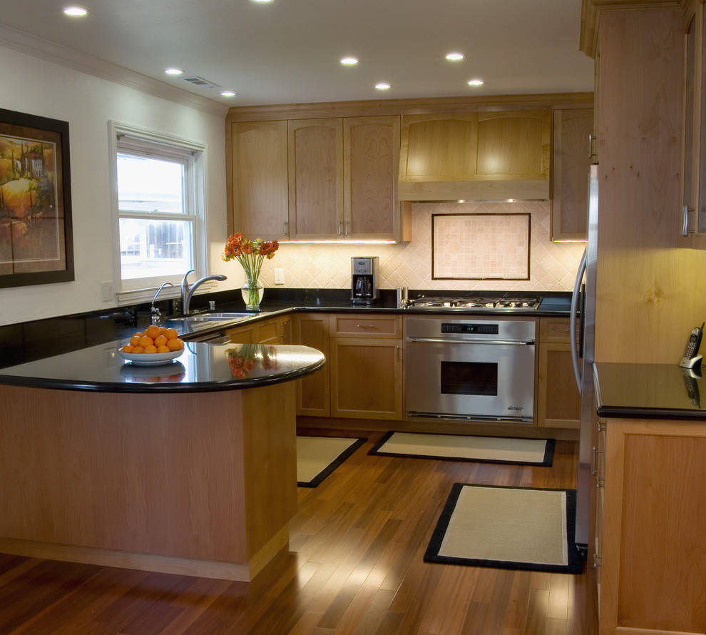 オマハにあるトラディショナルスタイルのおしゃれなキッチン (シルバーの調理設備、アンダーカウンターシンク、シェーカースタイル扉のキャビネット、中間色木目調キャビネット、ベージュキッチンパネル) の写真