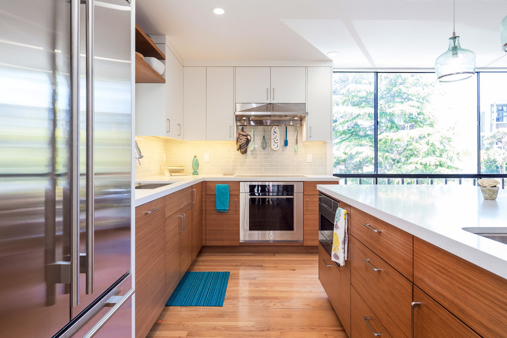 Idéer för ett mellanstort modernt vit l-kök, med en undermonterad diskho, släta luckor, vita skåp, bänkskiva i koppar, grått stänkskydd, stänkskydd i tunnelbanekakel, rostfria vitvaror, mellanmörkt trägolv, en köksö och brunt golv
