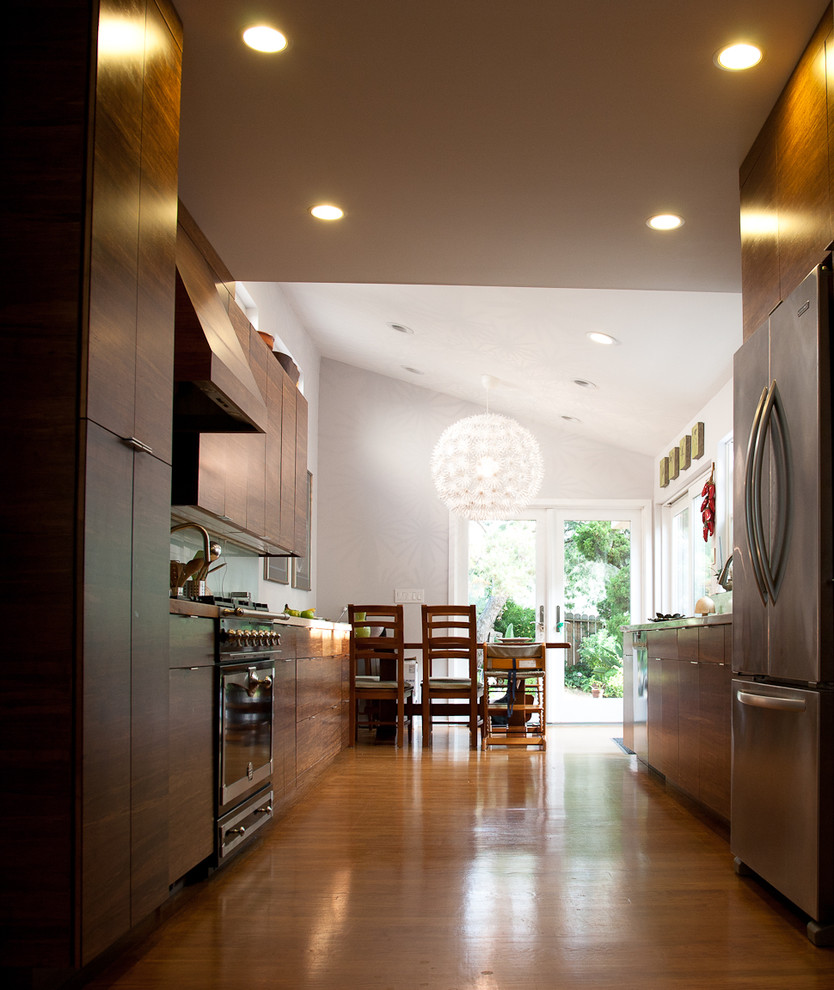 Cette photo montre une cuisine américaine parallèle tendance en bois brun de taille moyenne avec un sol en bois brun, un sol marron, un placard à porte plane, un électroménager en acier inoxydable et aucun îlot.