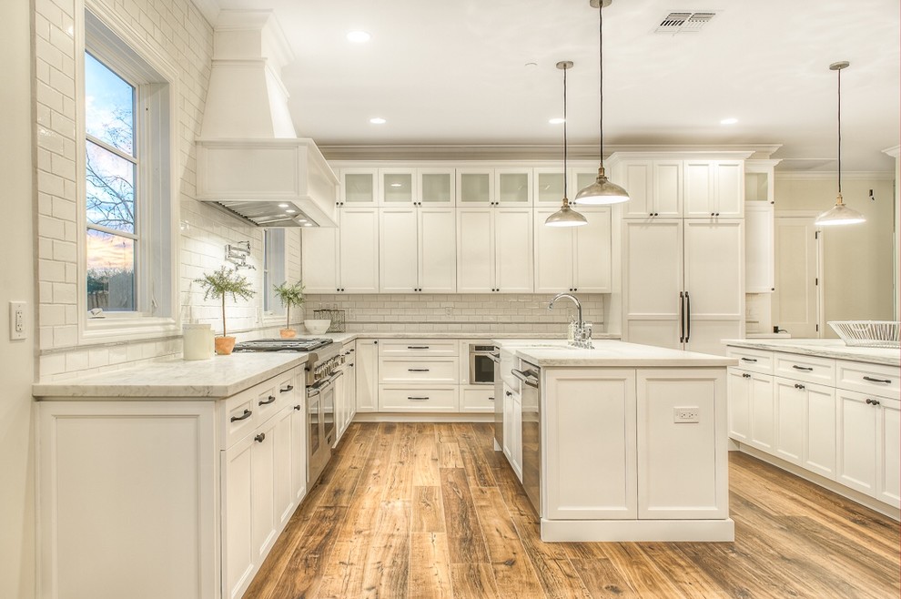 Eat-in kitchen - craftsman l-shaped medium tone wood floor eat-in kitchen idea in Phoenix with a farmhouse sink, white cabinets, marble countertops, white backsplash, subway tile backsplash, stainless steel appliances and two islands