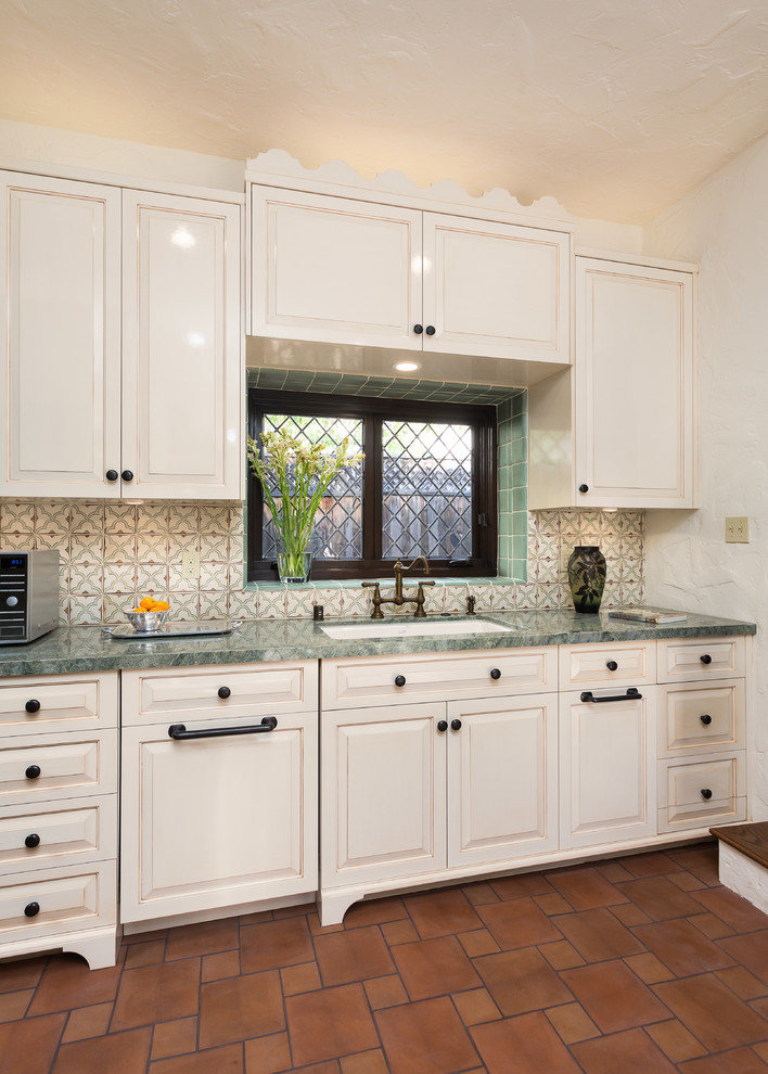 Example of a mid-sized tuscan single-wall terra-cotta tile and brown floor enclosed kitchen design in Los Angeles with an undermount sink, raised-panel cabinets, white cabinets, multicolored backsplash, marble countertops, ceramic backsplash and green countertops
