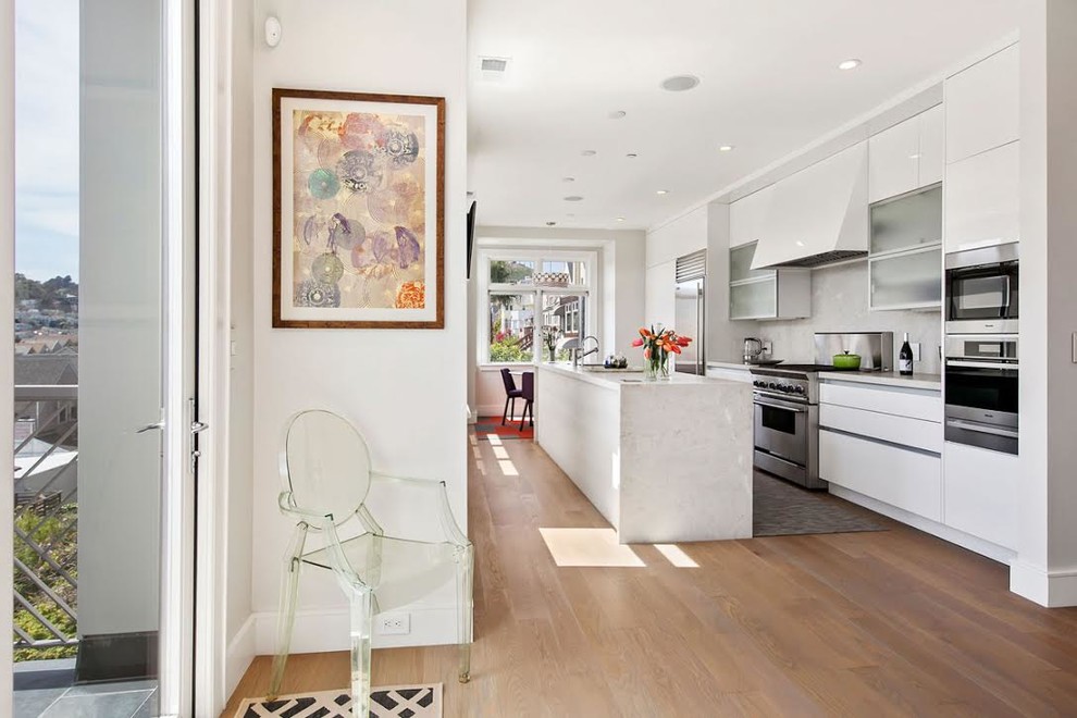 Inspiration for a mid-sized contemporary galley medium tone wood floor and brown floor eat-in kitchen remodel in San Francisco with flat-panel cabinets, white cabinets, stainless steel appliances, an island, an undermount sink, marble countertops, white backsplash and glass sheet backsplash