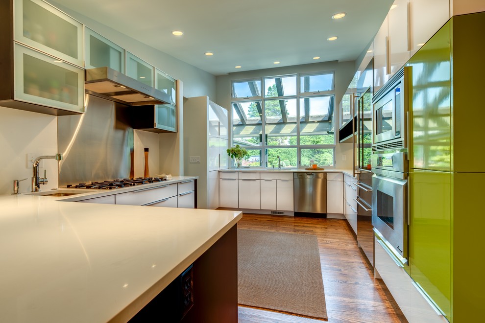 Example of a mid-sized trendy u-shaped medium tone wood floor kitchen pantry design in Seattle with an undermount sink, flat-panel cabinets, white cabinets, quartz countertops, white backsplash, stainless steel appliances and a peninsula