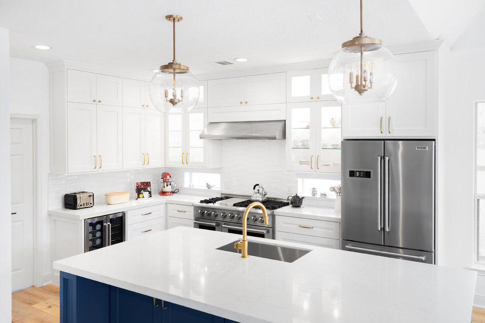 Inredning av ett klassiskt mellanstort vit vitt kök, med en undermonterad diskho, luckor med infälld panel, blå skåp, bänkskiva i kvarts, vitt stänkskydd, stänkskydd i tunnelbanekakel, rostfria vitvaror, ljust trägolv, en köksö och orange golv