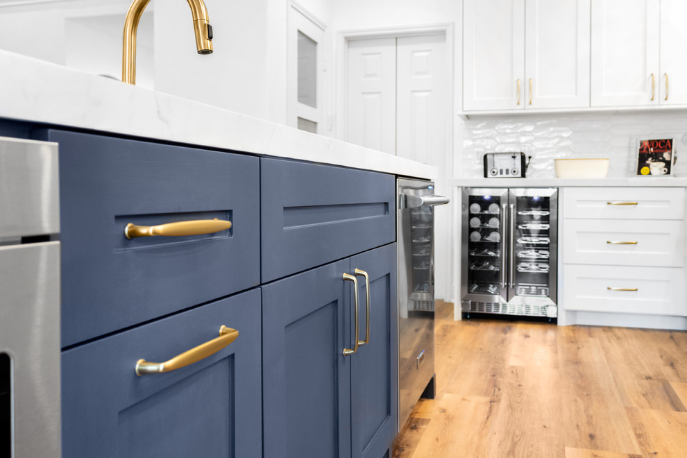 Mid-sized transitional l-shaped light wood floor and orange floor eat-in kitchen photo in Houston with an undermount sink, recessed-panel cabinets, blue cabinets, quartz countertops, white backsplash, subway tile backsplash, stainless steel appliances, an island and white countertops