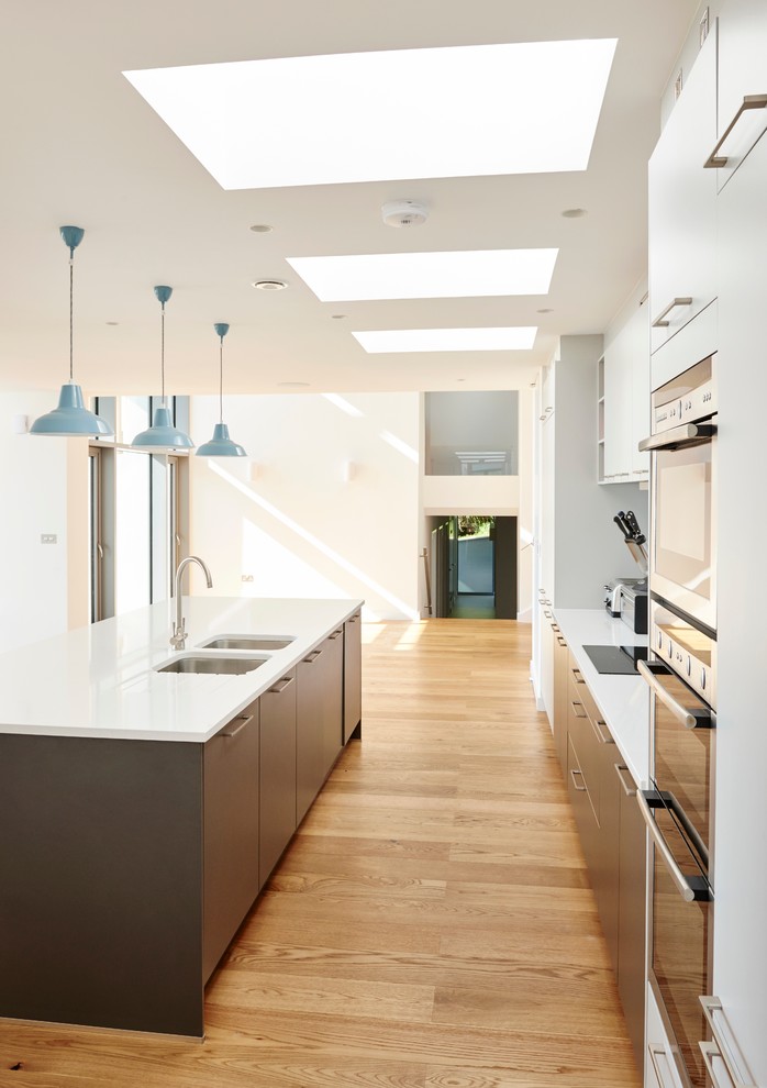 Design ideas for a medium sized contemporary galley open plan kitchen in Devon with an integrated sink, flat-panel cabinets, white cabinets, integrated appliances, medium hardwood flooring and an island.