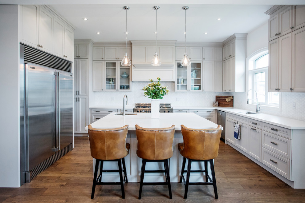 This is an example of a classic u-shaped kitchen in Toronto with a submerged sink, recessed-panel cabinets, grey cabinets, white splashback, stainless steel appliances, dark hardwood flooring, an island, brown floors and white worktops.