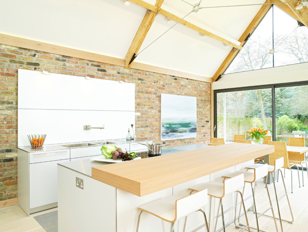Medium sized contemporary single-wall kitchen in Hampshire with a double-bowl sink, flat-panel cabinets, white cabinets, beige floors, wood worktops, white splashback, stainless steel appliances, light hardwood flooring and an island.