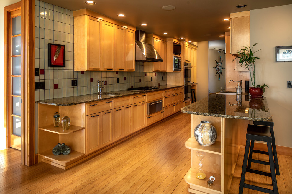 Inredning av ett eklektiskt mellanstort svart svart kök, med en undermonterad diskho, skåp i shakerstil, skåp i ljust trä, granitbänkskiva, grönt stänkskydd, stänkskydd i porslinskakel, rostfria vitvaror, bambugolv, en halv köksö och brunt golv