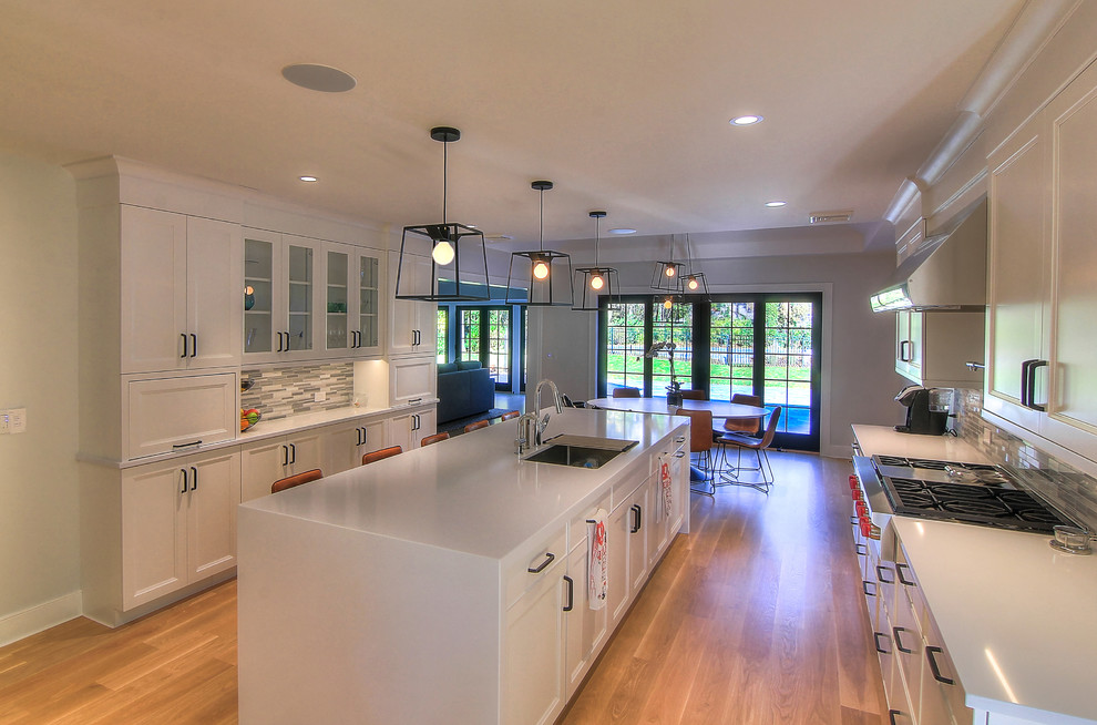 Large trendy galley light wood floor eat-in kitchen photo in New York with an undermount sink, flat-panel cabinets, white cabinets, solid surface countertops, blue backsplash, ceramic backsplash, stainless steel appliances and an island