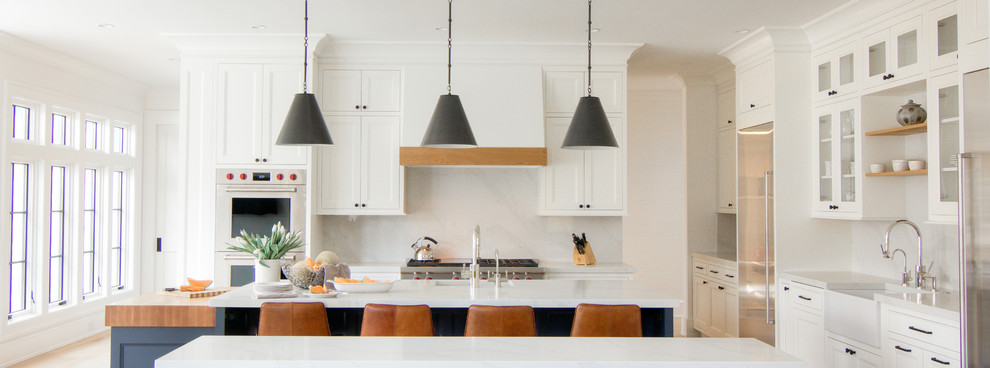 Example of a large transitional l-shaped light wood floor and yellow floor eat-in kitchen design in New York with a farmhouse sink, flat-panel cabinets, white cabinets, quartzite countertops, white backsplash, stone slab backsplash, stainless steel appliances, two islands and white countertops