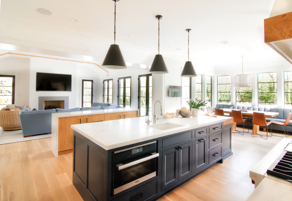 Example of a large transitional l-shaped light wood floor and yellow floor eat-in kitchen design in New York with a farmhouse sink, flat-panel cabinets, white cabinets, quartzite countertops, white backsplash, stone slab backsplash, stainless steel appliances, two islands and white countertops