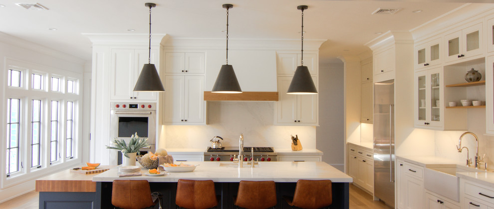Inspiration for a large transitional u-shaped light wood floor and yellow floor eat-in kitchen remodel in New York with a farmhouse sink, flat-panel cabinets, white cabinets, quartzite countertops, white backsplash, stone slab backsplash, stainless steel appliances, two islands and white countertops