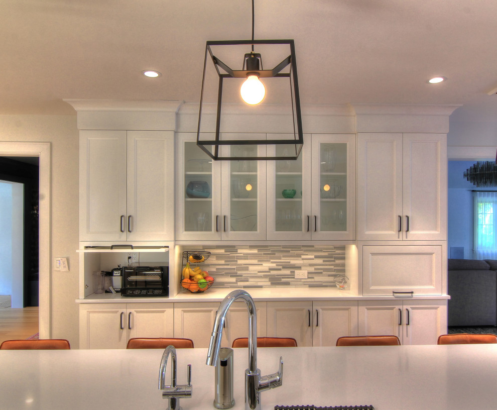Cette photo montre une cuisine américaine parallèle tendance avec un évier encastré, des portes de placard blanches, une crédence grise, un électroménager en acier inoxydable, parquet clair et îlot.
