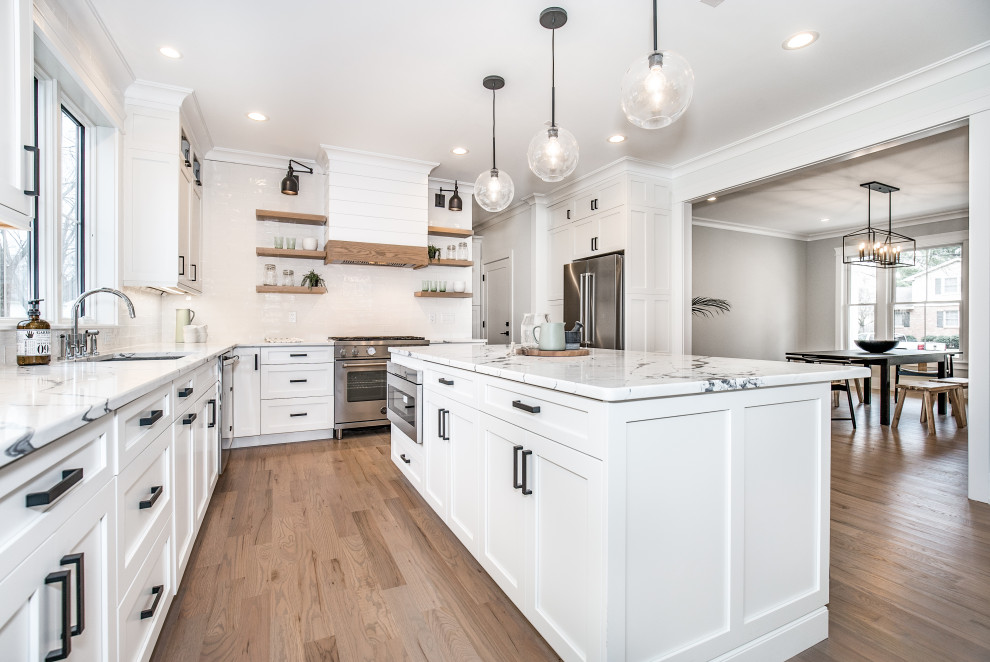 Design ideas for a classic l-shaped kitchen in New York with a submerged sink, shaker cabinets, white cabinets, white splashback, stainless steel appliances, medium hardwood flooring, an island, brown floors and white worktops.